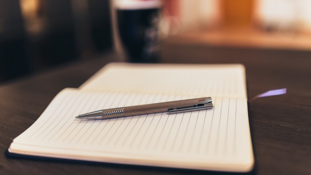 A notepad with a pen on top of it, and a black coffee cup in the background.